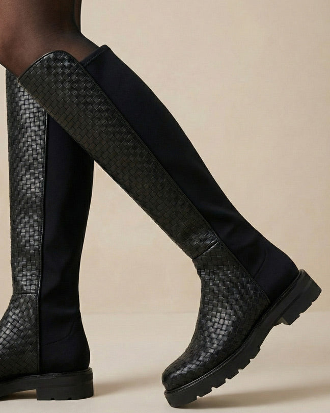 Black knee-high boots with woven pattern and chunky sole on neutral background
