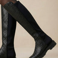 Black knee-high boots with woven pattern and chunky sole on neutral background