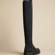 Black knee-high boot with textured pattern and thick sole on neutral background