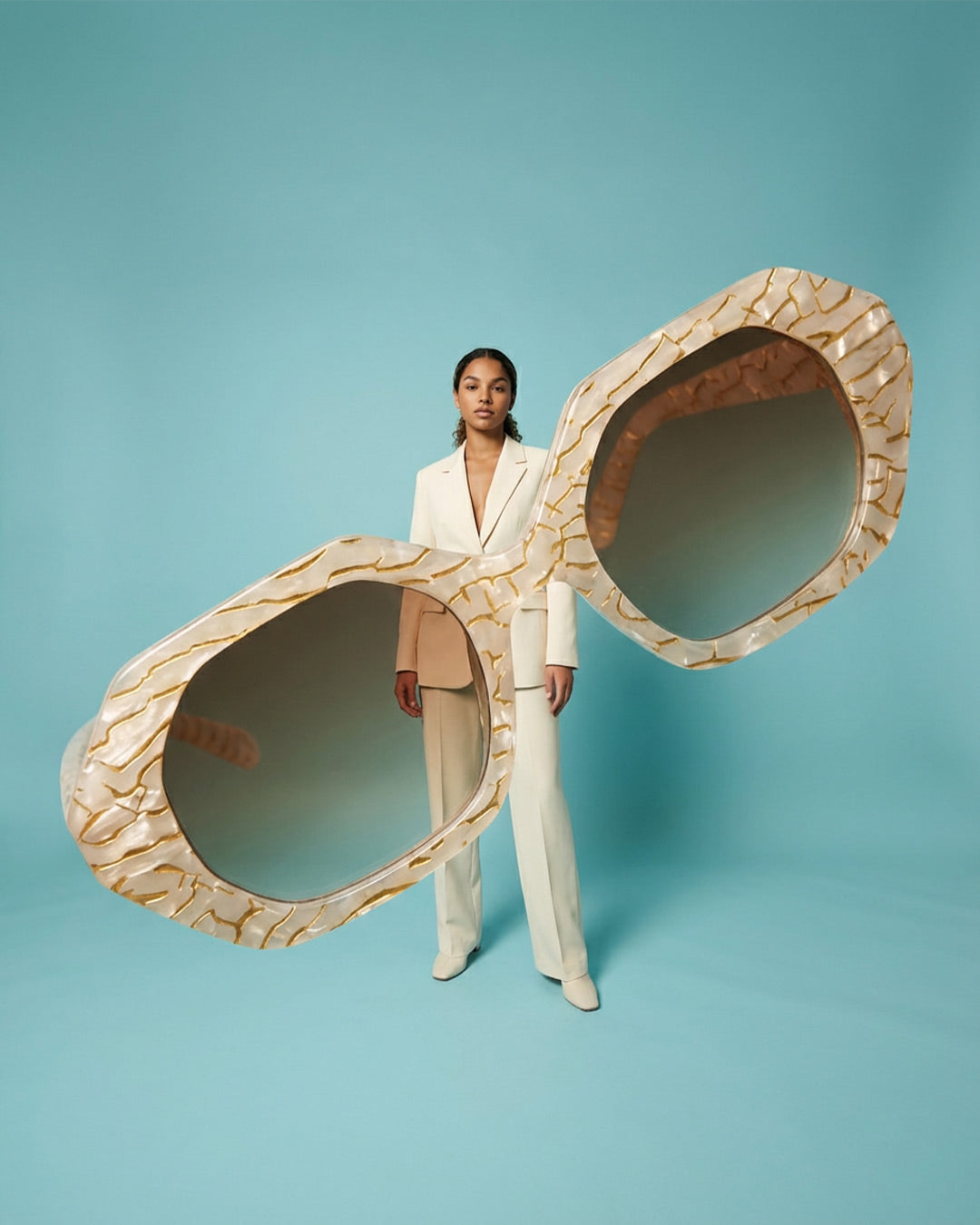 Woman in white suit posing with oversized textured sunglasses on blue background
