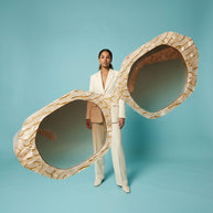 Woman in white suit posing with oversized textured sunglasses on blue background