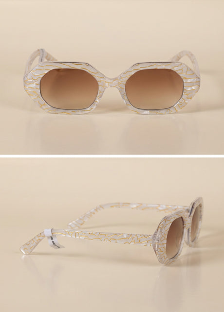 Geometric sunglasses with clear gold-patterned frames and brown gradient lenses on beige background