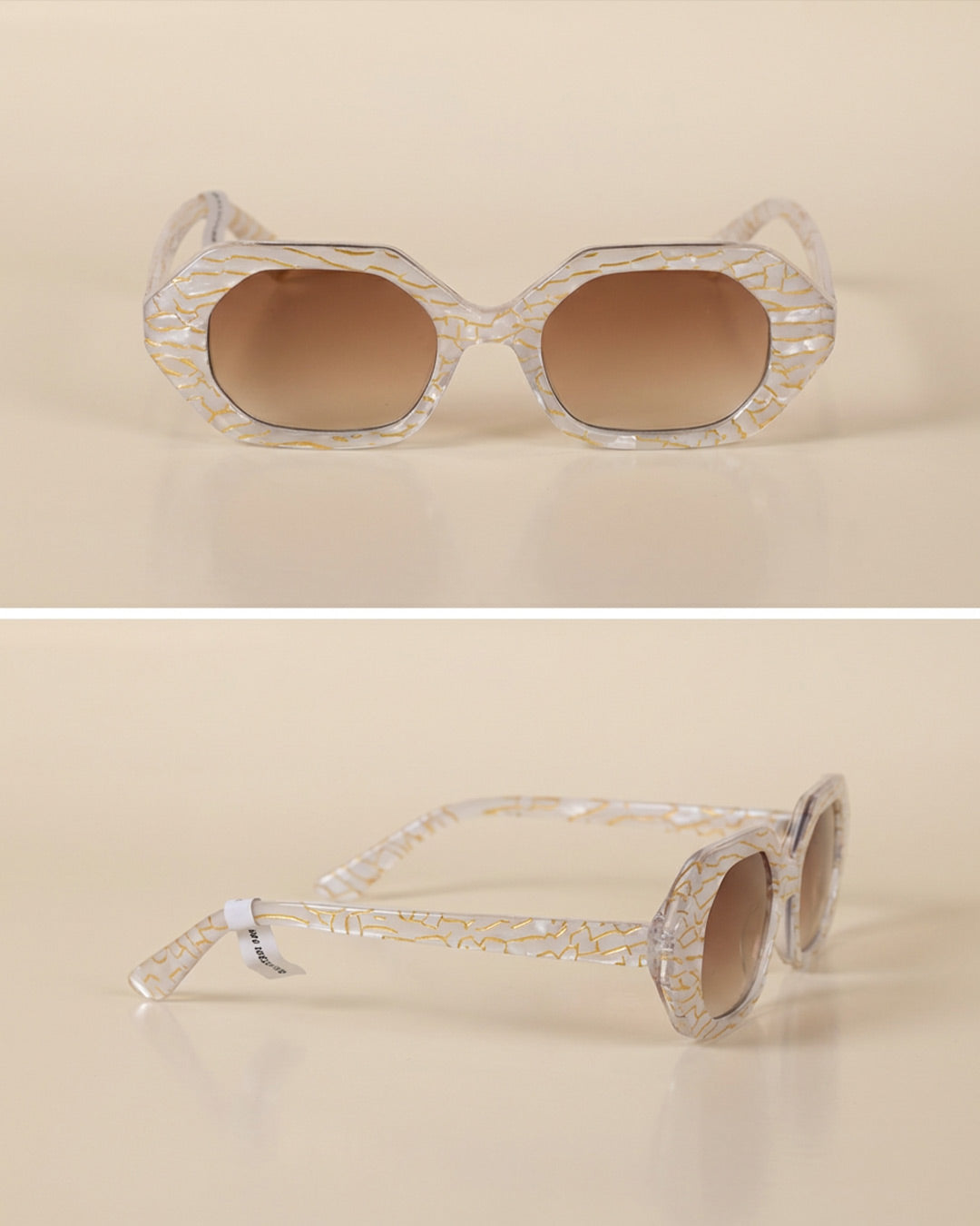 Geometric sunglasses with clear gold-patterned frames and brown gradient lenses on beige background