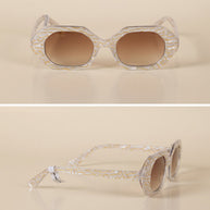 Geometric sunglasses with clear gold-patterned frames and brown gradient lenses on beige background