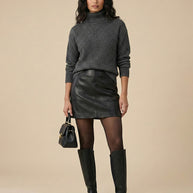 Woman modeling dark grey turtleneck sweater, black leather mini skirt, knee-high boots, black handbag