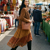 Woman in boho dress and fringe jacket with woven bag shopping at outdoor market