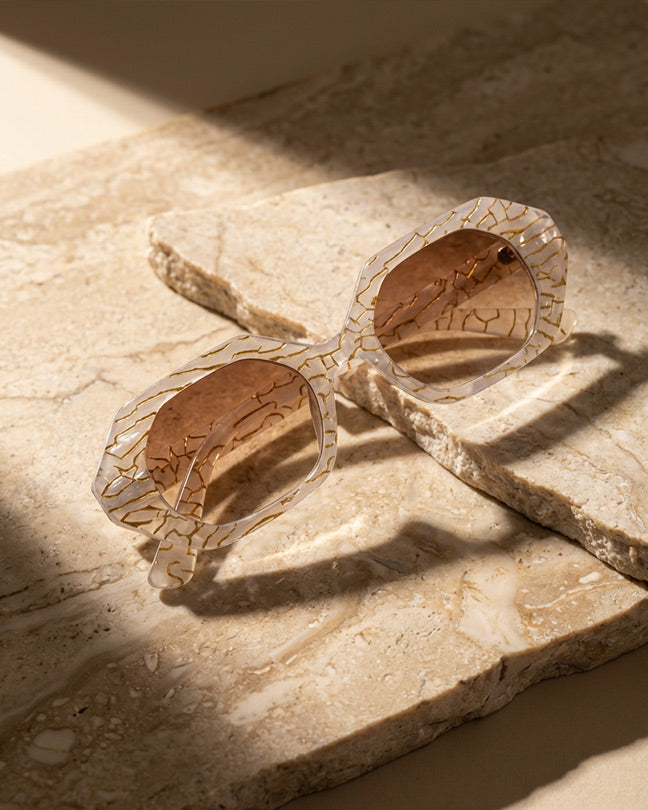 Beige geometric sunglasses with brown tinted lenses on textured stone surface in sunlight