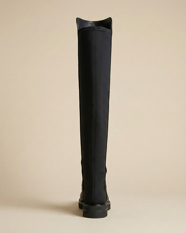 Black knee-high boot with flat sole, rear view, on neutral background