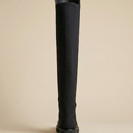 Black knee-high boot with flat sole, rear view, on neutral background