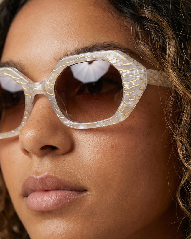 Woman wearing oversized geometric sunglasses with marbled white and gold frames