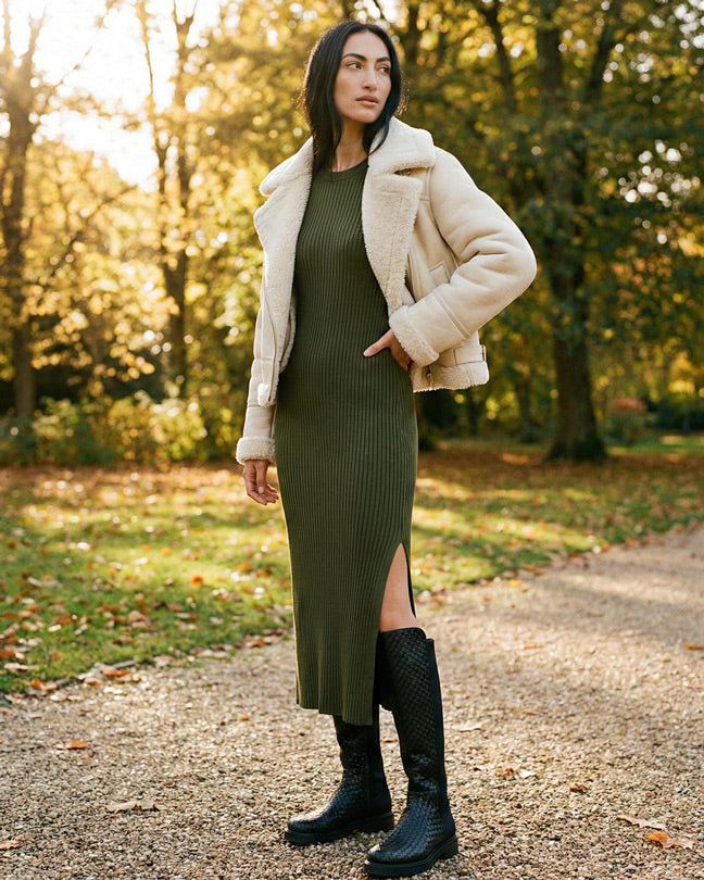 Woman in olive ribbed midi dress, shearling jacket, and black boots outdoors in autumn