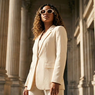 Woman in cream blazer and matching pants with sunglasses stands by neoclassical columns
