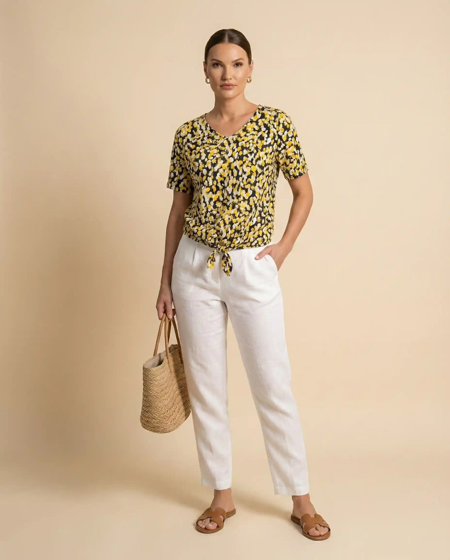 Woman wearing yellow patterned blouse with white pants, holding straw tote bag