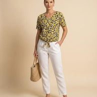 Woman wearing yellow patterned blouse with white pants, holding straw tote bag
